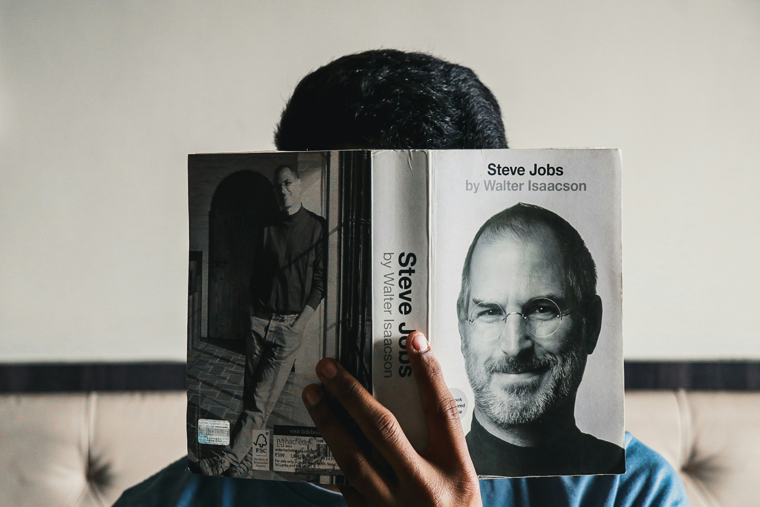 Person hält das Buch Steve Jobs von Walter Isaacson, wobei das Buch das Gesicht von Steve Jobs auf dem Cover zeigt. Der Hintergrund ist unscharf und die Person ist teilweise sichtbar.