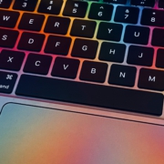 Nahaufnahme einer MacBook-Tastatur mit bunten Lichtern, die die Tasten in verschiedenen Farben erleuchten.