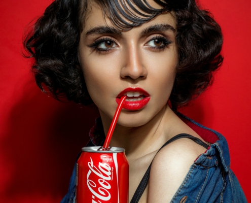 Markenbotschafterin mit Coca-Cola-Dose vor rotem Hintergrund, trinkt mit Strohhalm
